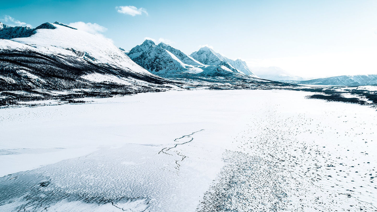 A frozen Norwegian fjord, with snow-capped mountains looming in the background on a clear winter day