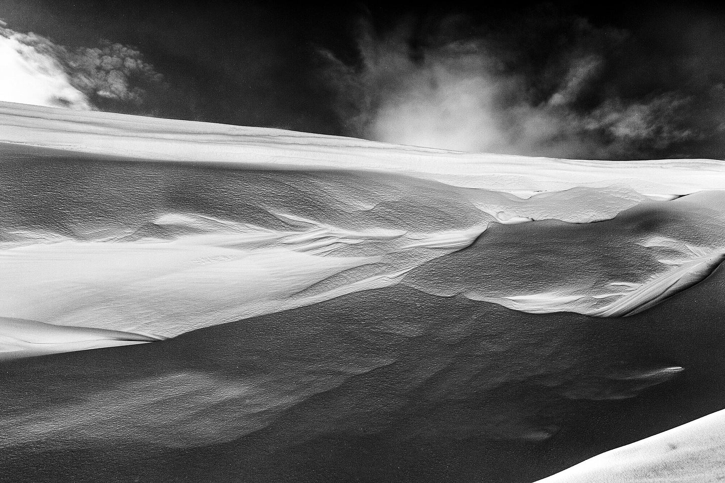 Black and white photograph capturing a detailed view of a wind-sculpted snowy ravine wall in the Arctic wilderness.