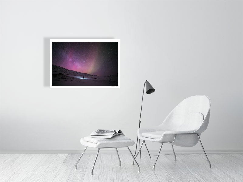 Photo print of person gazing at stars in Arctic wilderness, pink aurora borealis, white living room wall.