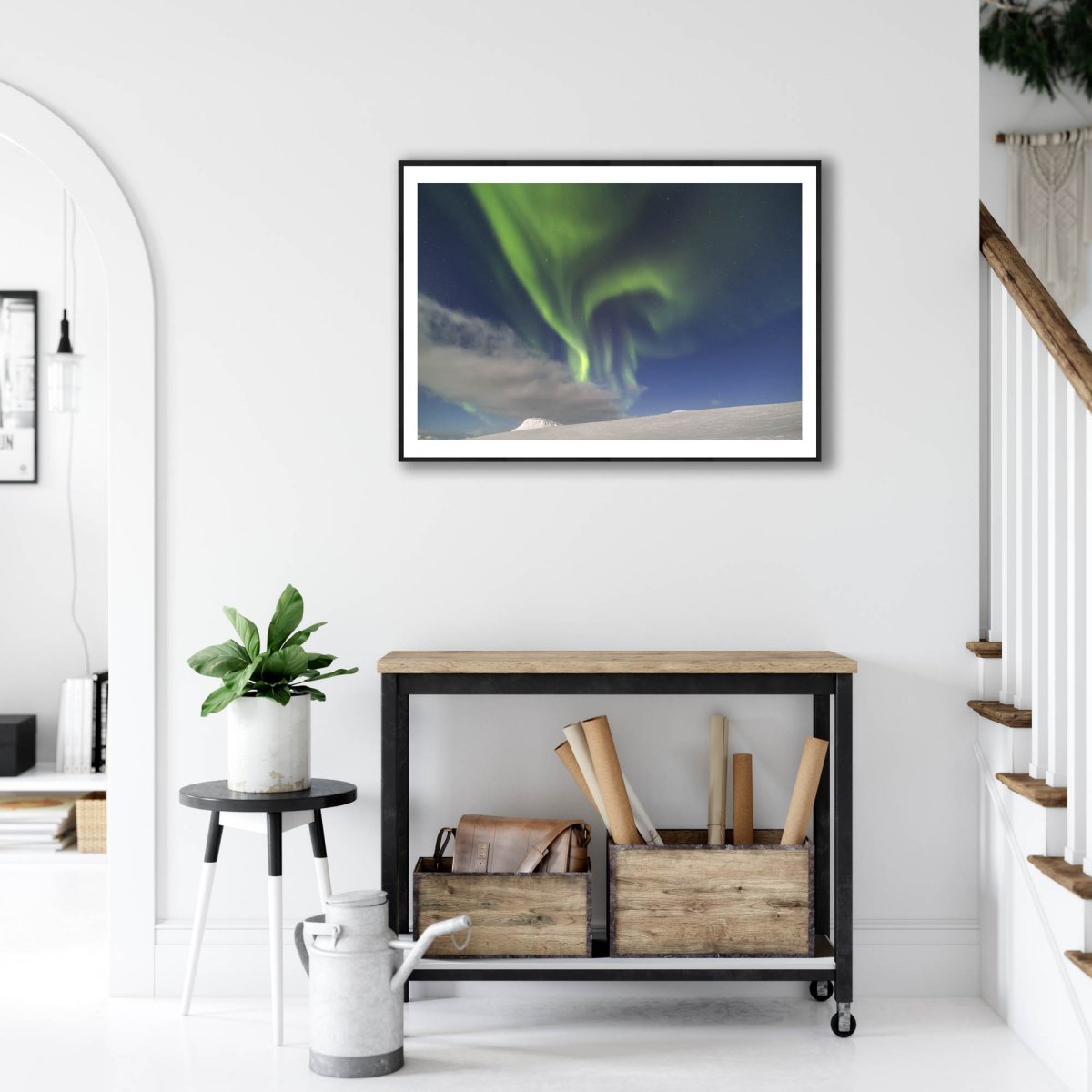 Art print of mountains, moonlight, cloud, Northern Lights & stars, black-framed on white wall above desk.