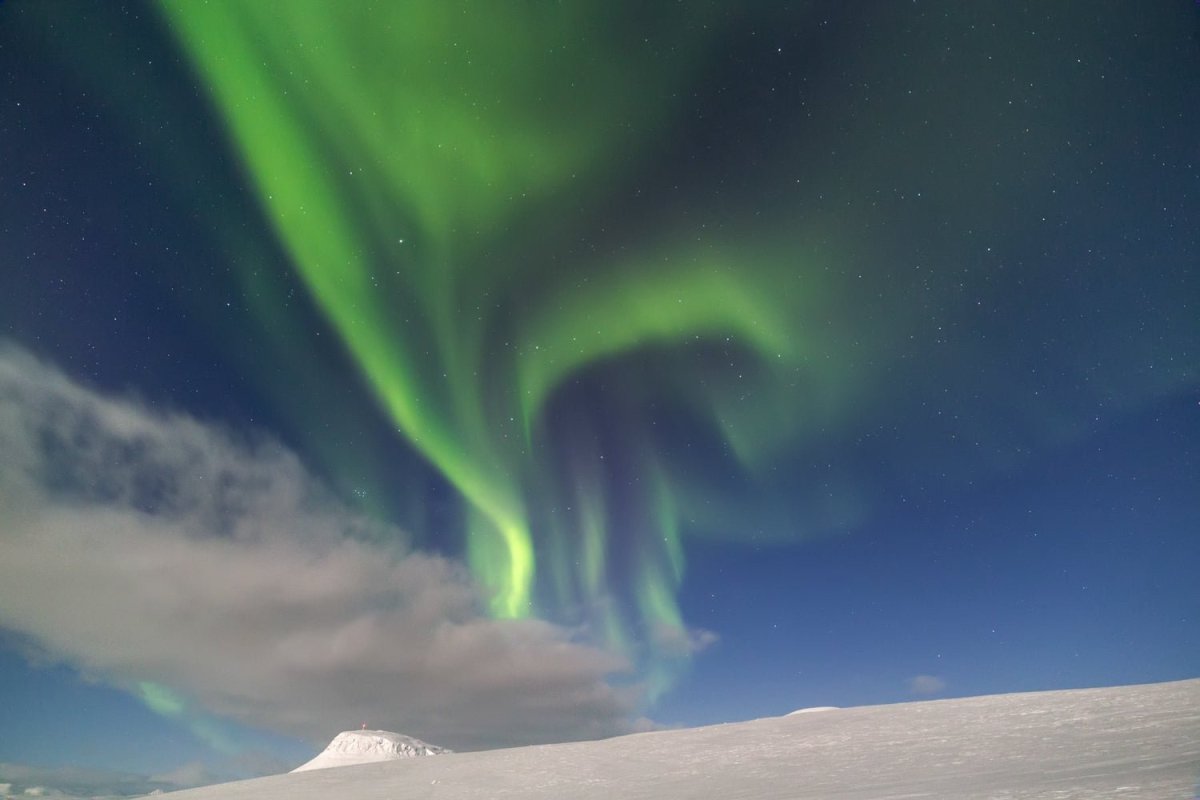 Arctic landscape with snow mountains in moonlight, thin cloud, and Northern Lights. Stars peek through gaps.