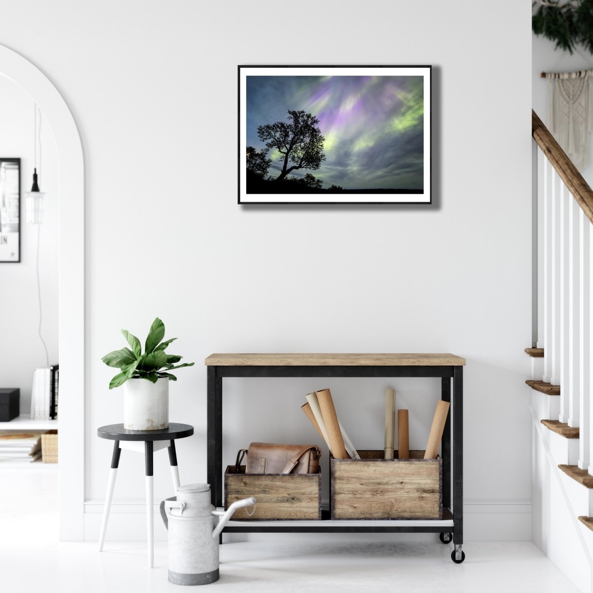 Fine art print of mountain birch tree silhouetted against Auroras, black-framed, on white living room wall above desk.