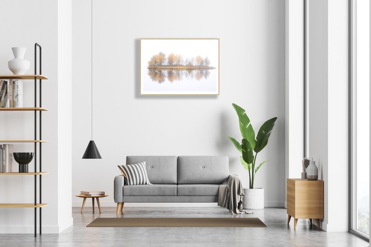 Fine art print of autumn island on foggy lake, oak frame on white wall above sofa.