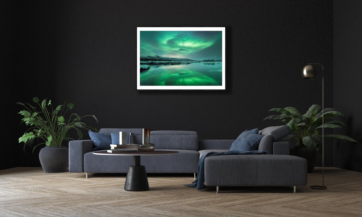 Fine art print of Northern Lights and mountains reflecting in lake, on black wall above living room sofa.