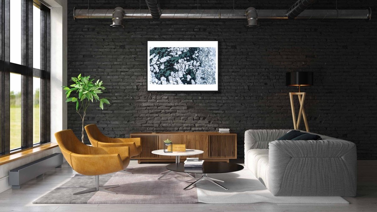 Framed aerial photo, Norwegian Sea, seabed visible between shards of ice, black brick living room wall.