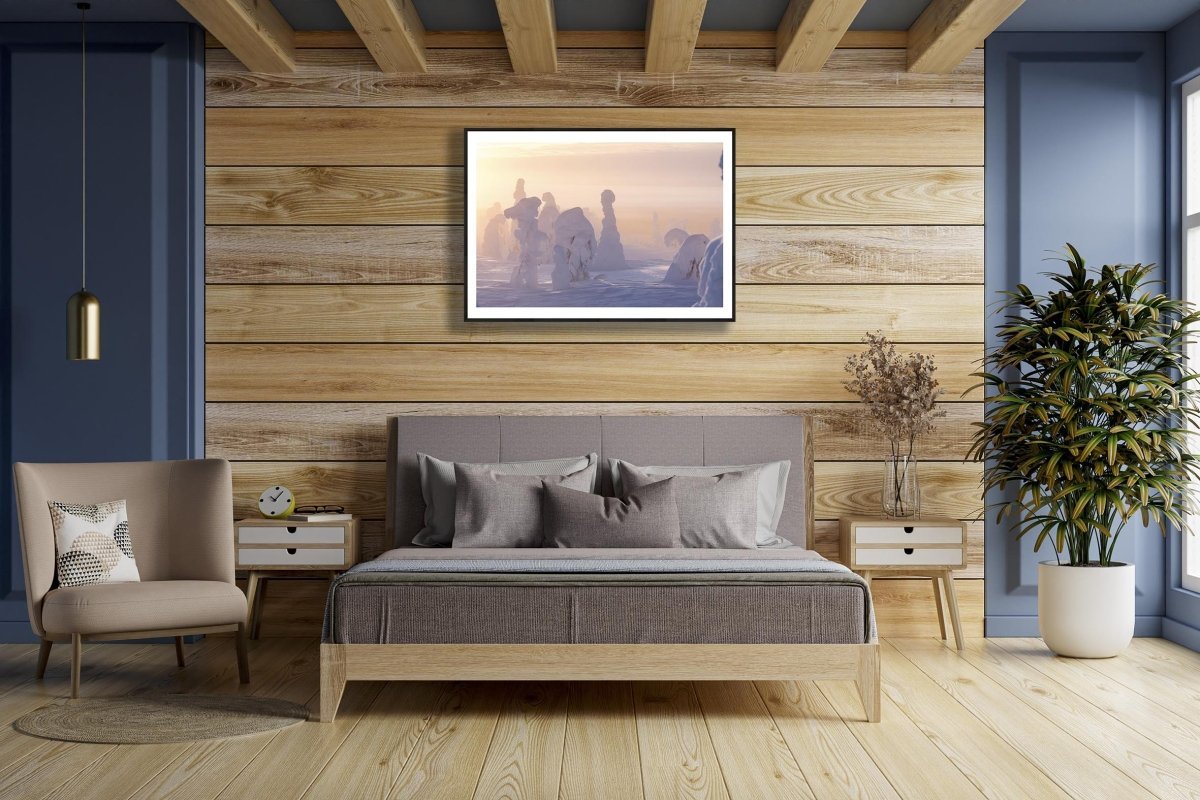 Framed photo of snowy trees on misty fell, sun shining through fog, wooden bedroom wall.