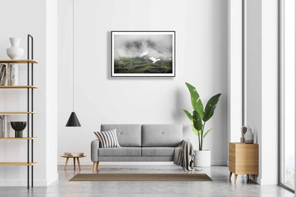 Framed photo of cloud-covered Norwegian peak with meltwater streams, snowy patches, white living room wall.