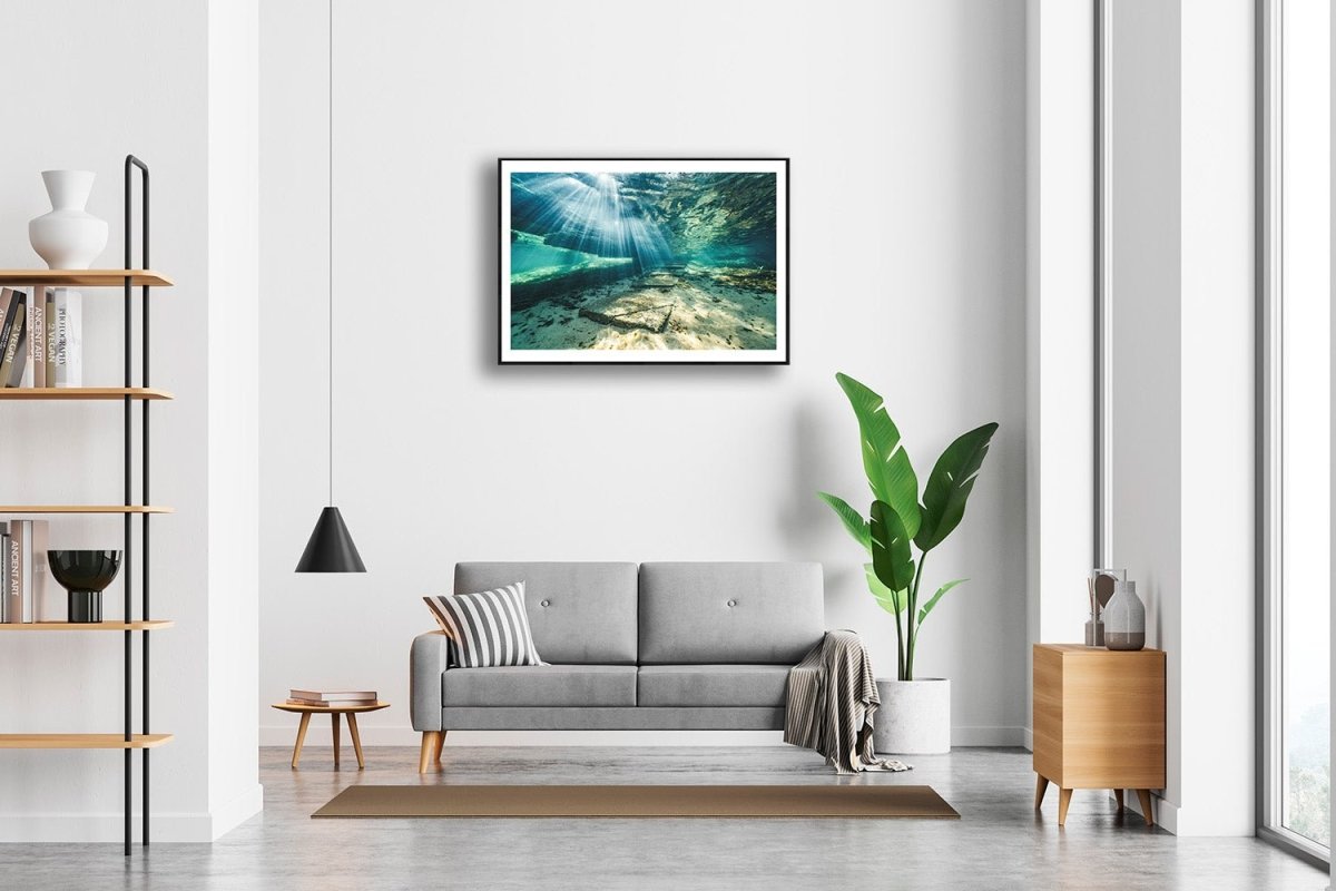 Framed photo of sunlight shining through water, illuminating underwater steps, white living room wall.