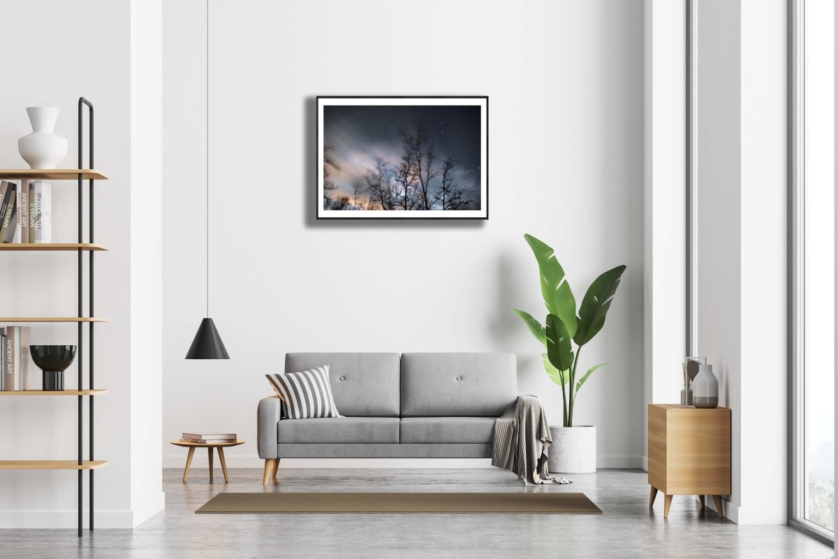 Framed winter storm long exposure photo of swaying trees, rushing clouds, and fixed stars, white living room wall.