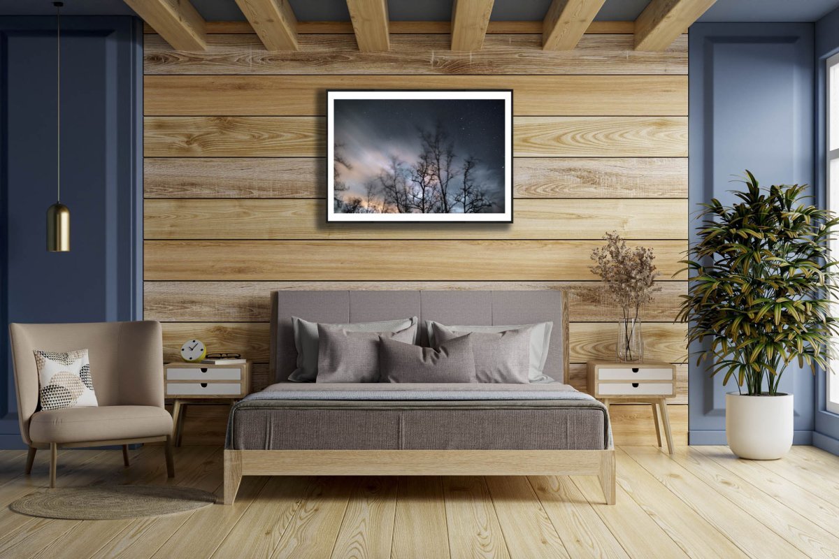 Framed winter storm long exposure photo of swaying trees, rushing clouds, and fixed stars, wooden bedroom wall.