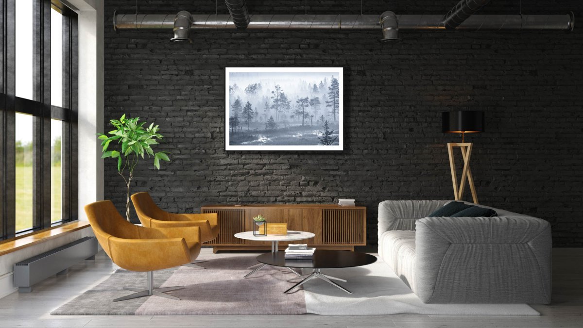 Framed photo of dense morning fog shrouding grassy marshland and forest, tree crowns visible, black brick living room wall.