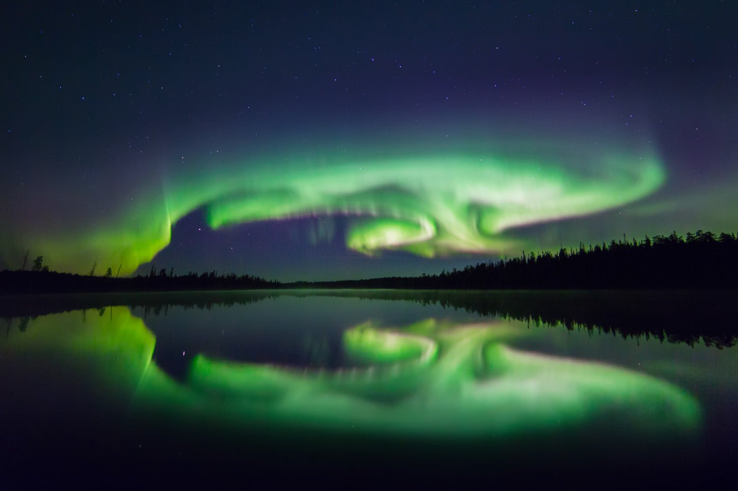Photo from a lake shore with Northern Lights reflecting as turtle shapes in the water.
