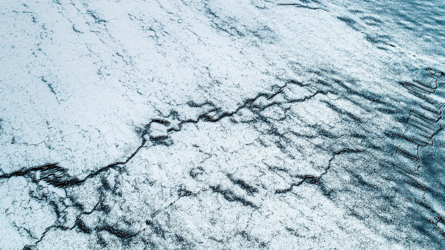 Aerial view from Norway; the ocean is frozen and has cracked, creating a striking graphic pattern on the ice's surface