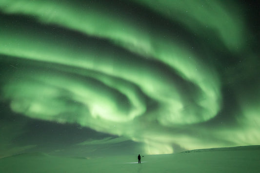 Person staring at massive green auroras in Arctic wilderness.