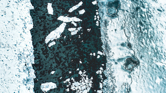Aerial view of an icy fjord in Norway, with the sea thawed in the middle and shattered ice floes scattered around.
