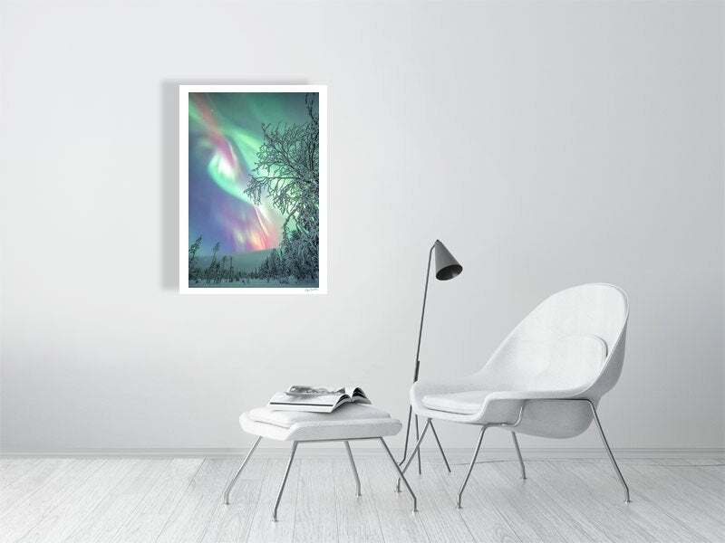 Fine art photography print of Aurora borealis over snowy forest displayed on white living room wall.