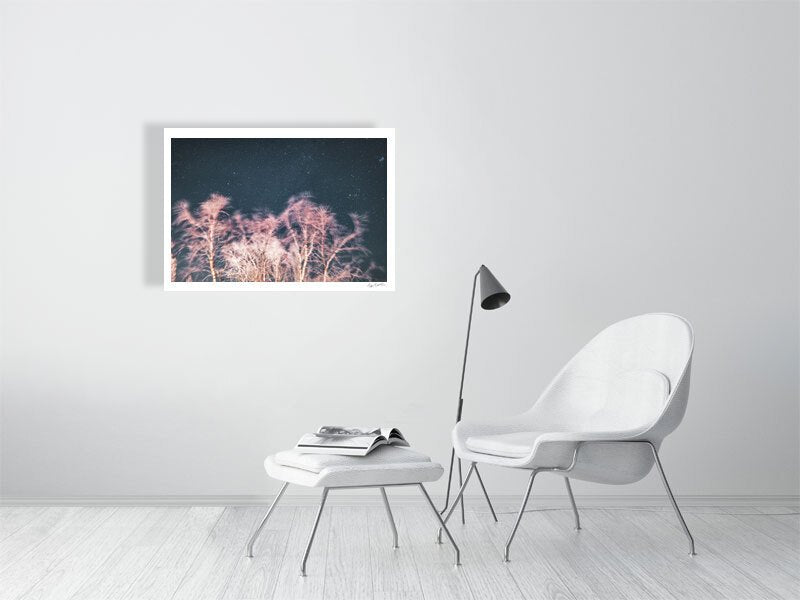 Photo print of long exposure winter storm photo with swaying trees and starry sky, reddish light, white living room wall.