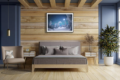 Fine art photography print of Moonlit auroras dancing over snowy trees, black-framed, on wooden bedroom wall above bed.