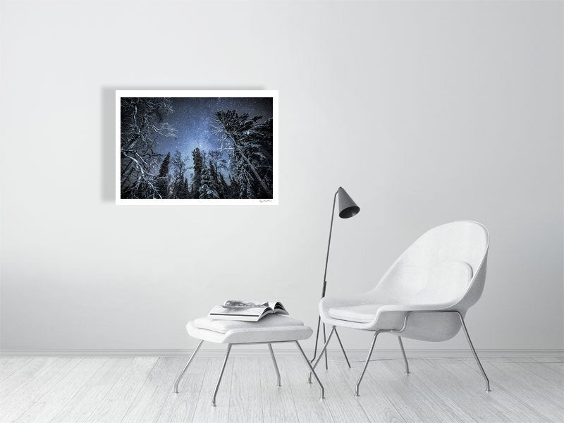 Photo print of illuminated trees in a winter forest under a starry sky, displayed on a white wall in a living room.