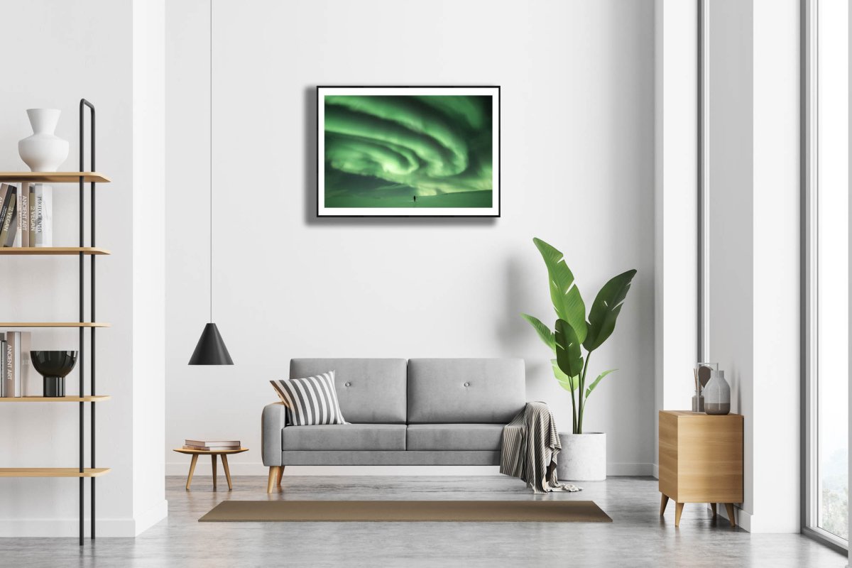 Framed photo of person staring at massive green auroras in Arctic wilderness, white living room wall.