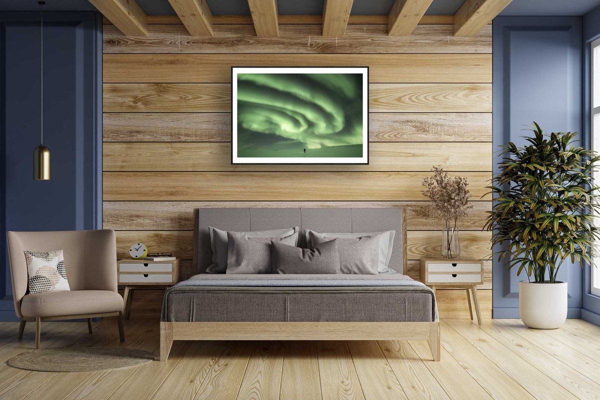 Framed photo of person staring at massive green auroras in Arctic wilderness, wooden bedroom wall.