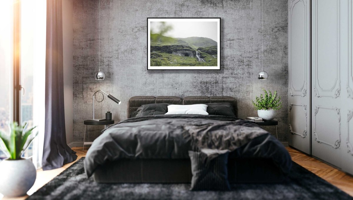 Black-framed photo of Norwegian river winding past cave entrance in lush green mountains, grey stone bedroom wall.
