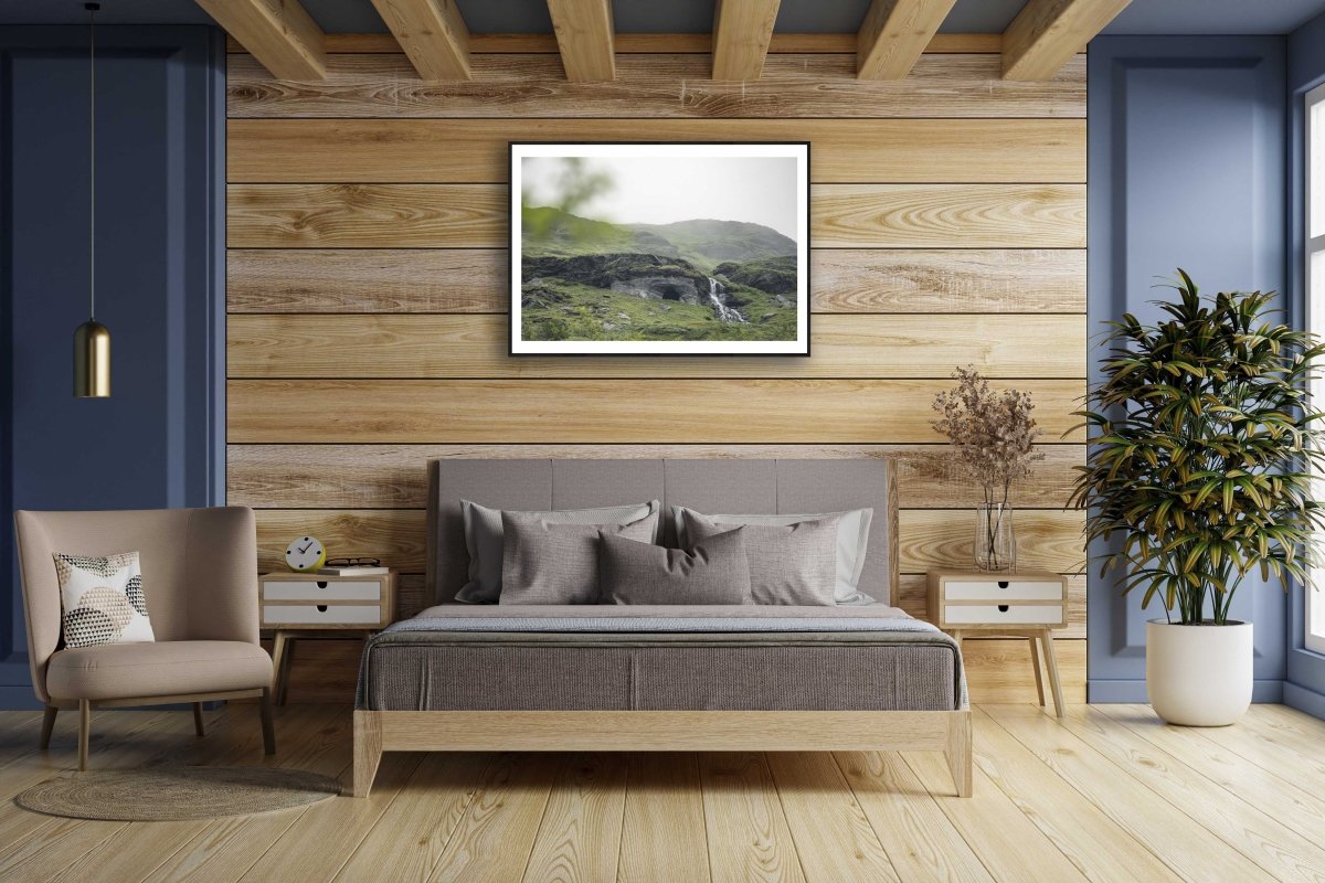 Framed photo of Norwegian river winding past cave entrance in lush green mountains, wooden bedroom wall.