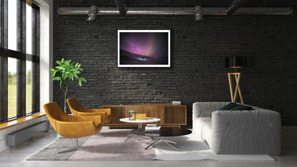 Framed photo of person gazing at stars in Arctic wilderness, pink aurora borealis, black brick living room wall.