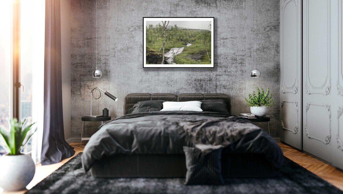 Norwegian river meanders through green mountains on cloudy day, black-framed print on grey stone wall above bed.