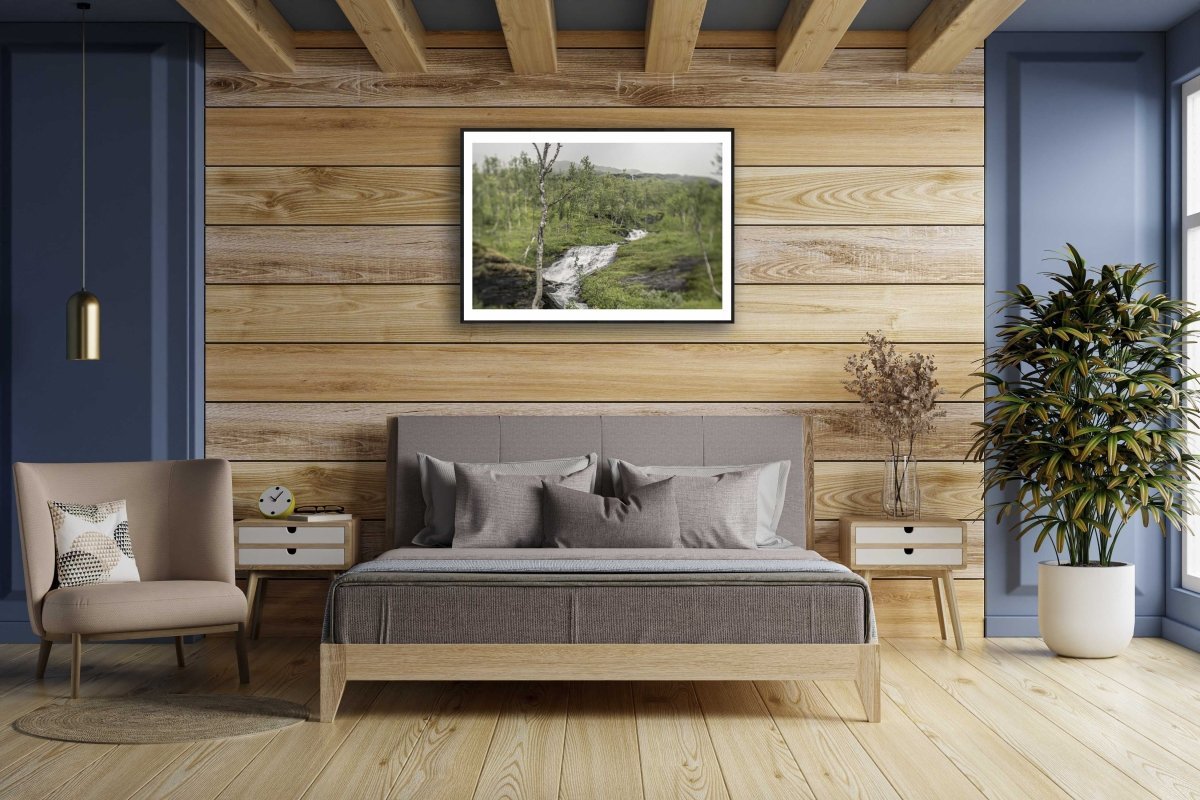 Framed Norwegian river print on wooden wall above bed, mountains in background.