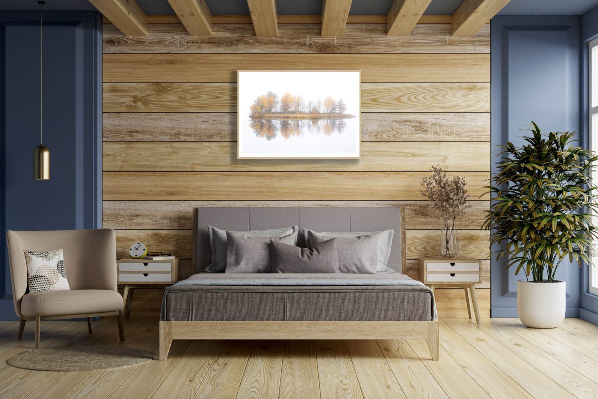 Fine art print of misty lake with autumn island, oak framed on wooden wall above bed.