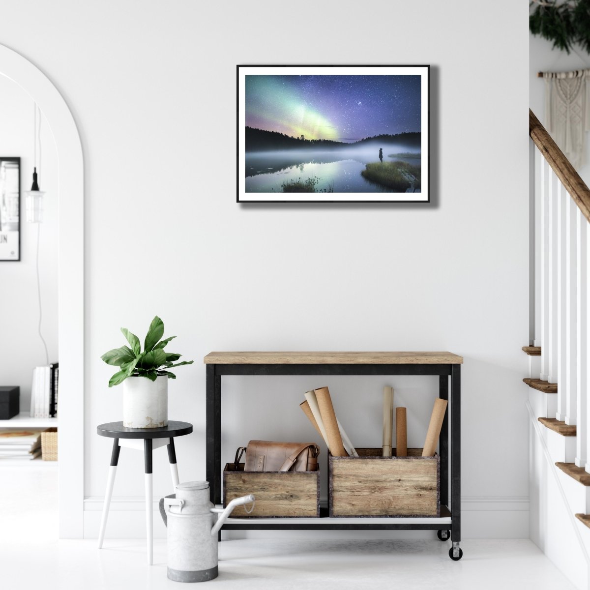 Fine art photography print of person in forest at night, reflecting Northern Lights and stars, black-framed on white wall.