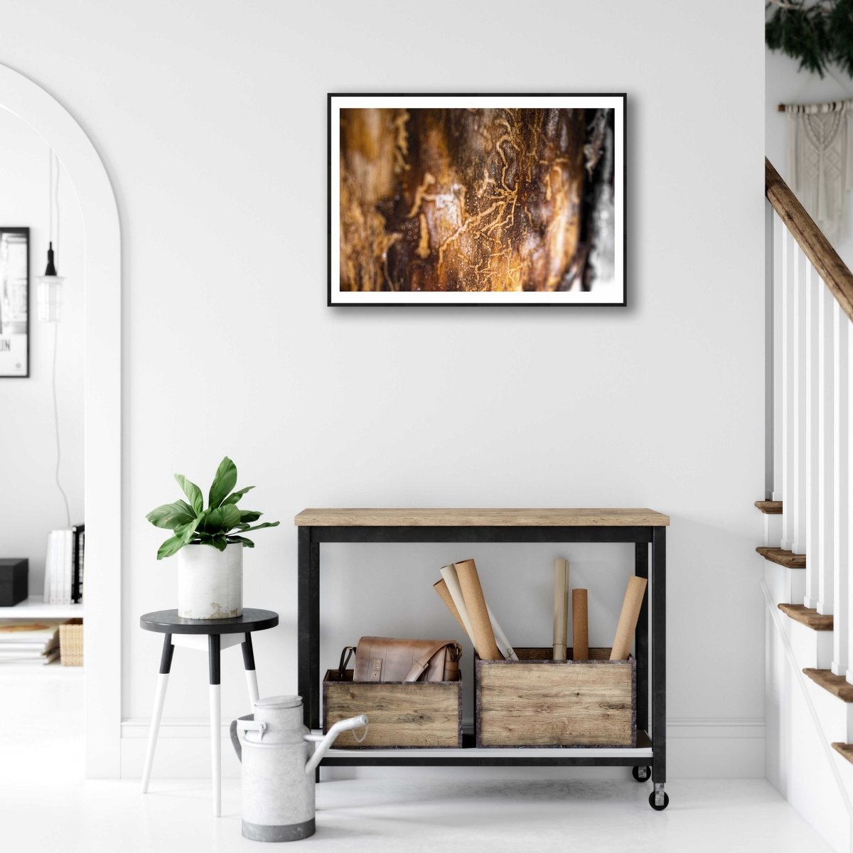 Framed art print of a close-up tilt-shift image of bark beetle tracks, on a white wall above a small desk in a living room.