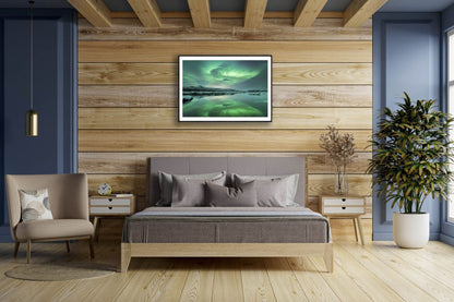 Fine art print of Northern Lights and mountains reflecting in lake, on wooden wall above bed.