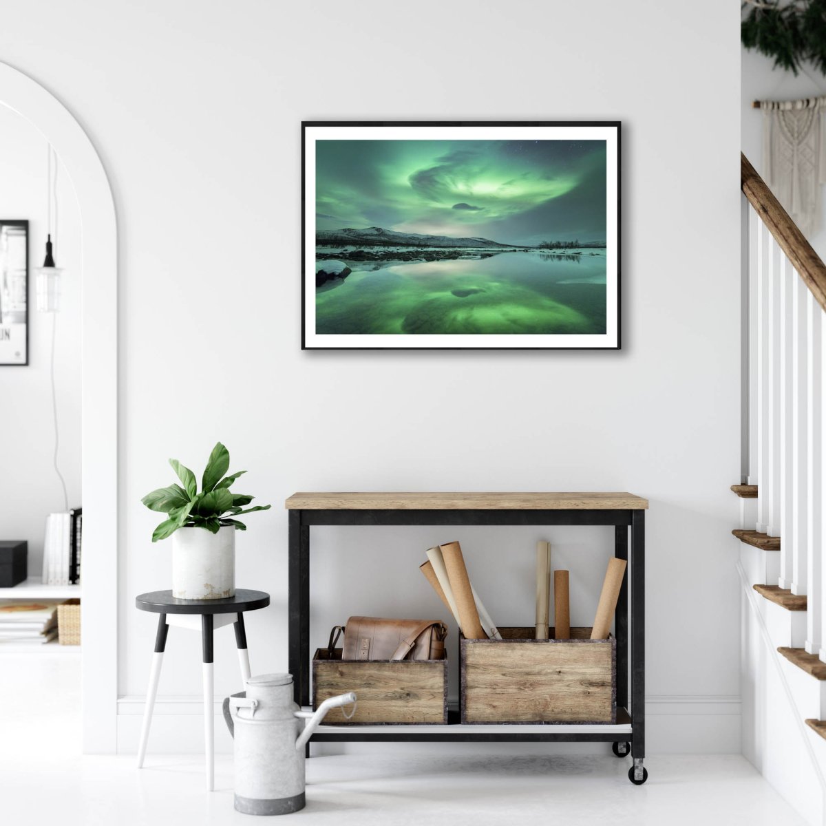 Fine art print of Northern Lights and mountains reflecting in lake, on white wall above desk.