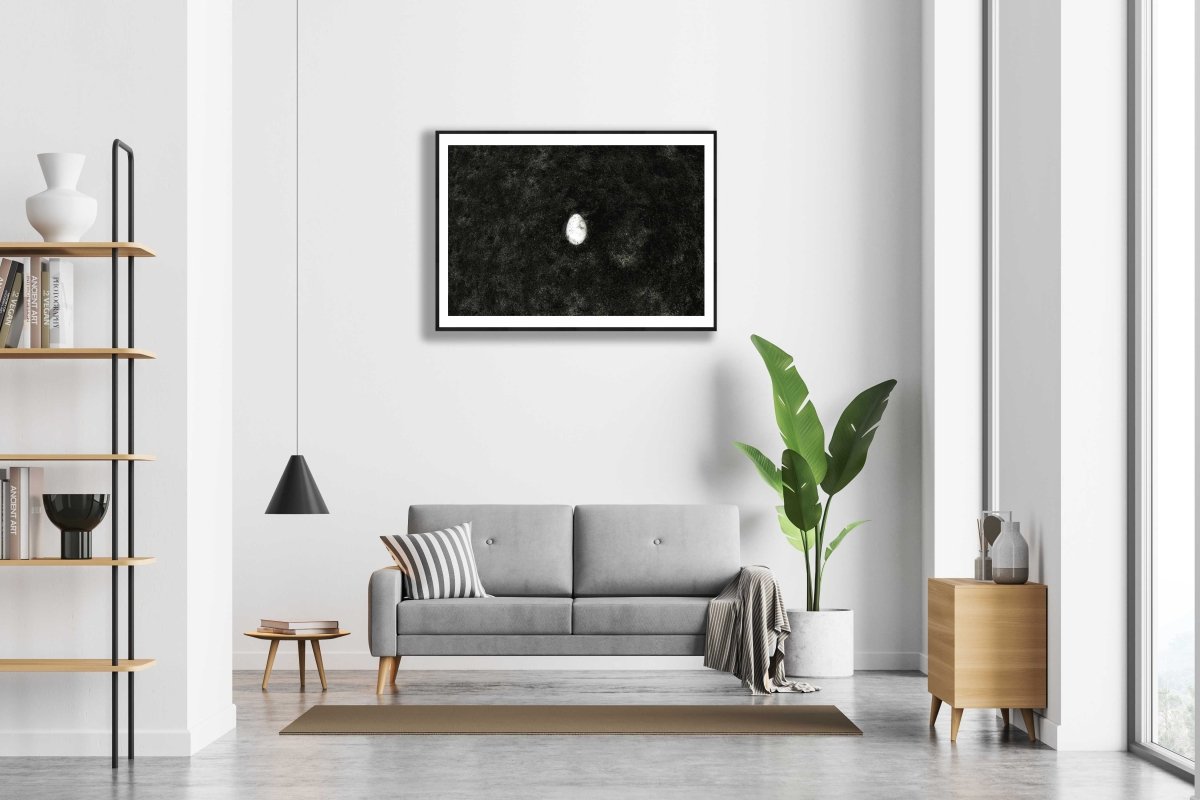  Framed fine art print of a broken egg lying at the bottom of the lake, on a white wall above a sofa in a modern living room.