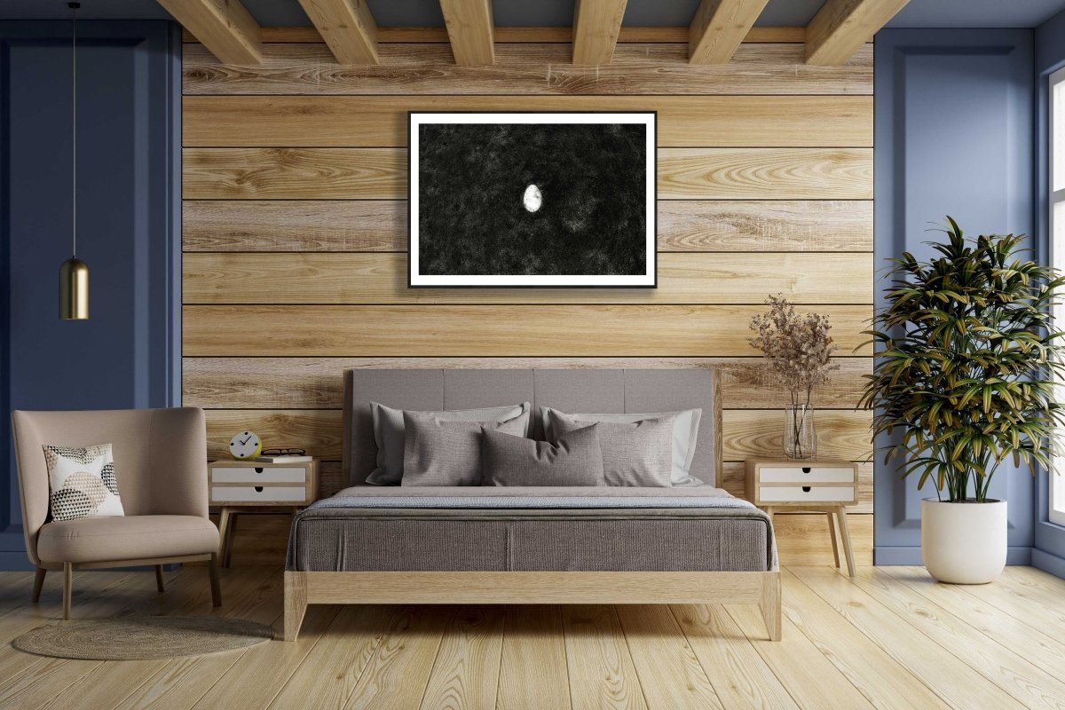 Framed fine art print of a broken egg lying at the bottom of the lake, and is hung on a wooden wall above a bed in a bedroom.