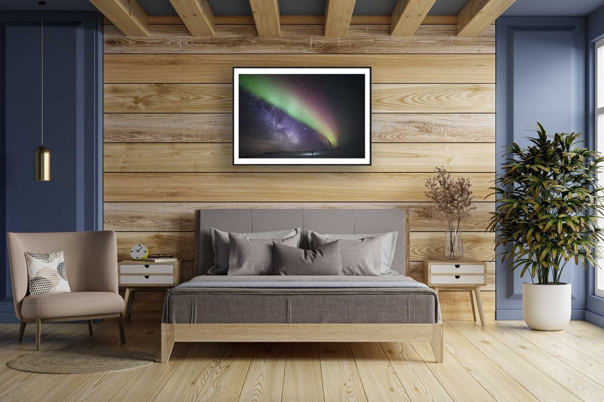 Framed Arctic wilderness aurora Milky Way print, person gazing, wooden wall.