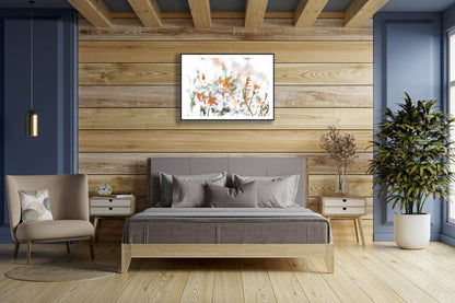 Fine art print of snowy blueberry bushes with autumn leaves in a black wood frame, hung on a wooden wall above a bed.