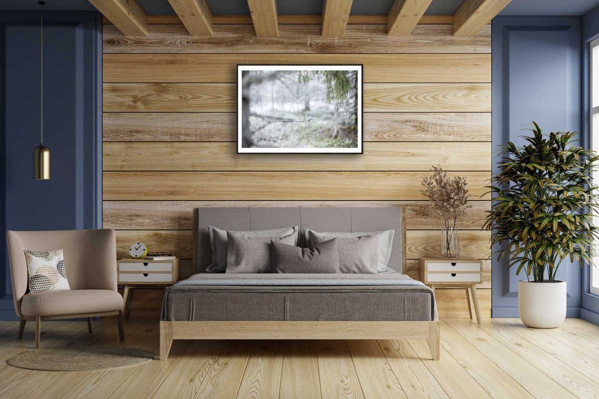 Framed print of a tilt-shift image of a frosted spruce forest in early winter on a wooden wall above a bed in a bedroom.