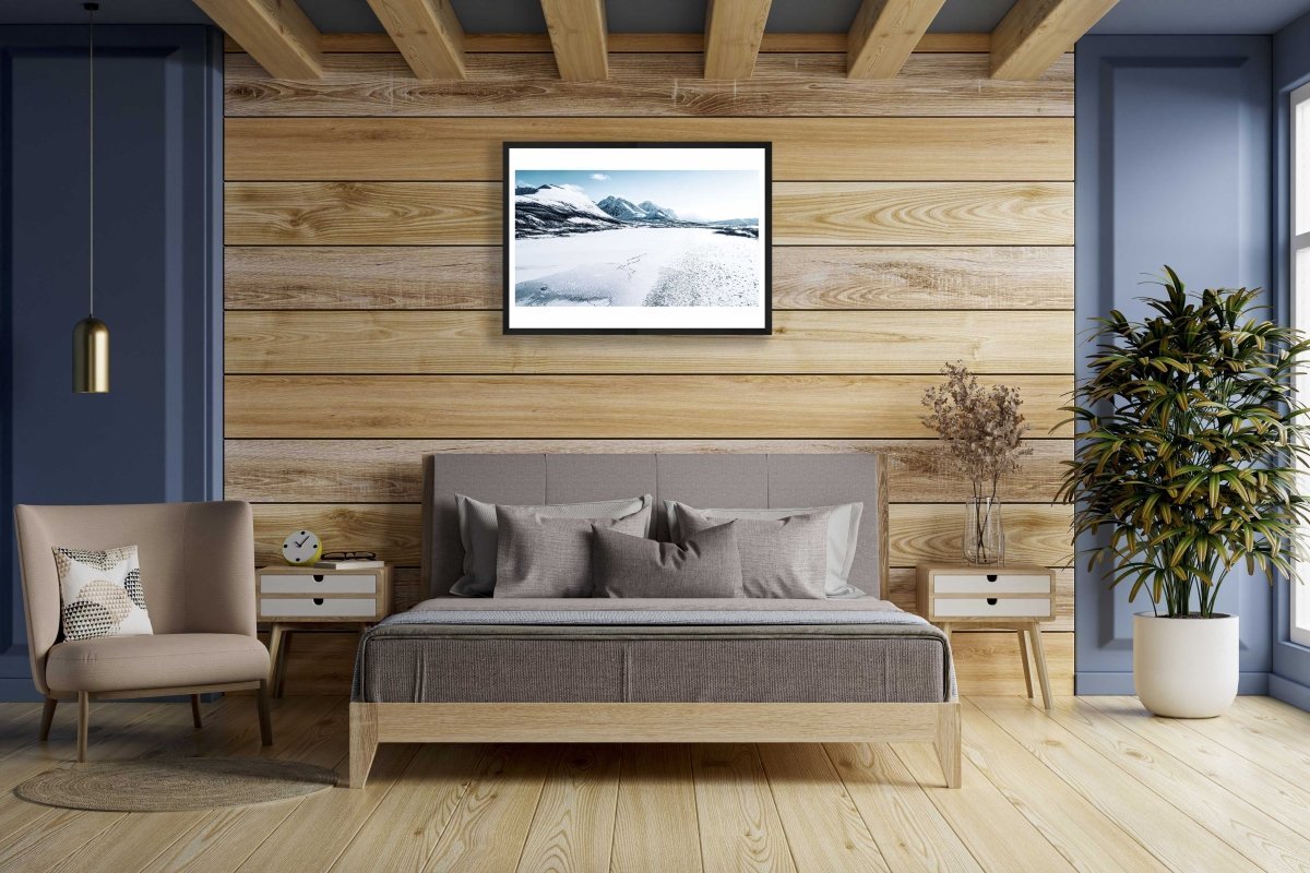 Framed frozen Norwegian fjord photo, snow-capped mountains in background, wooden bedroom wall.