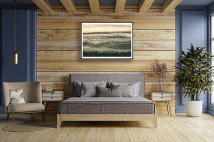 Framed aerial photo of northern forest shrouded in mist and clouds, morning sunlight, wooden bedroom wall.
