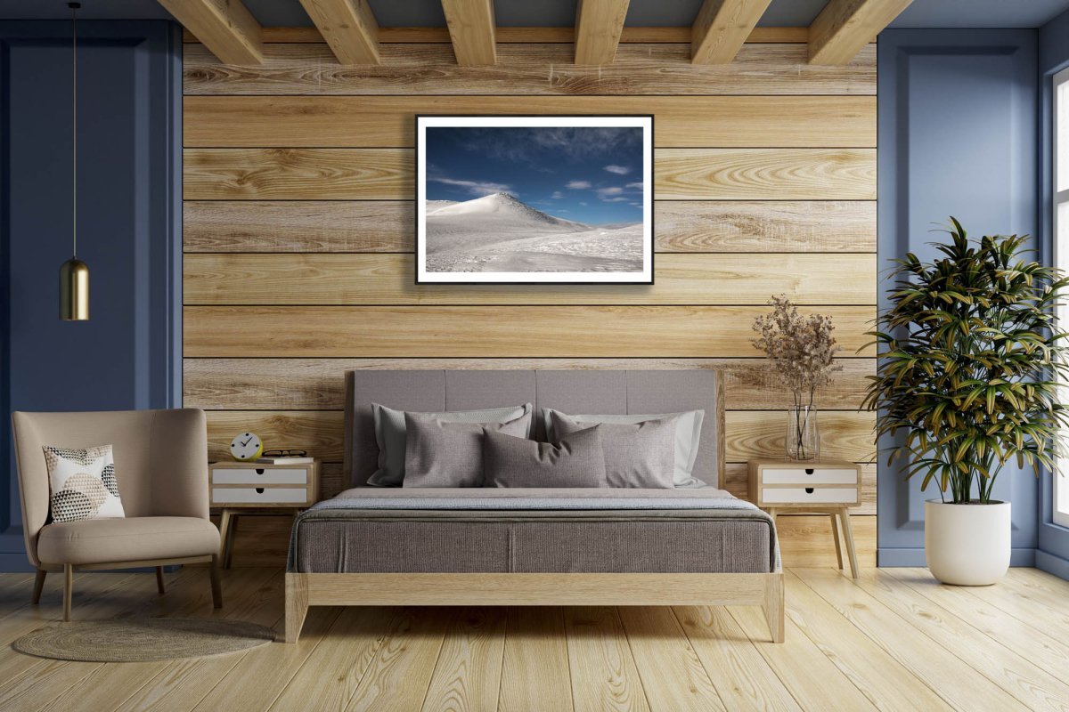 Fine art photography print of arctic highland with moonlit snow, framed on wooden wall above bedroom bed.