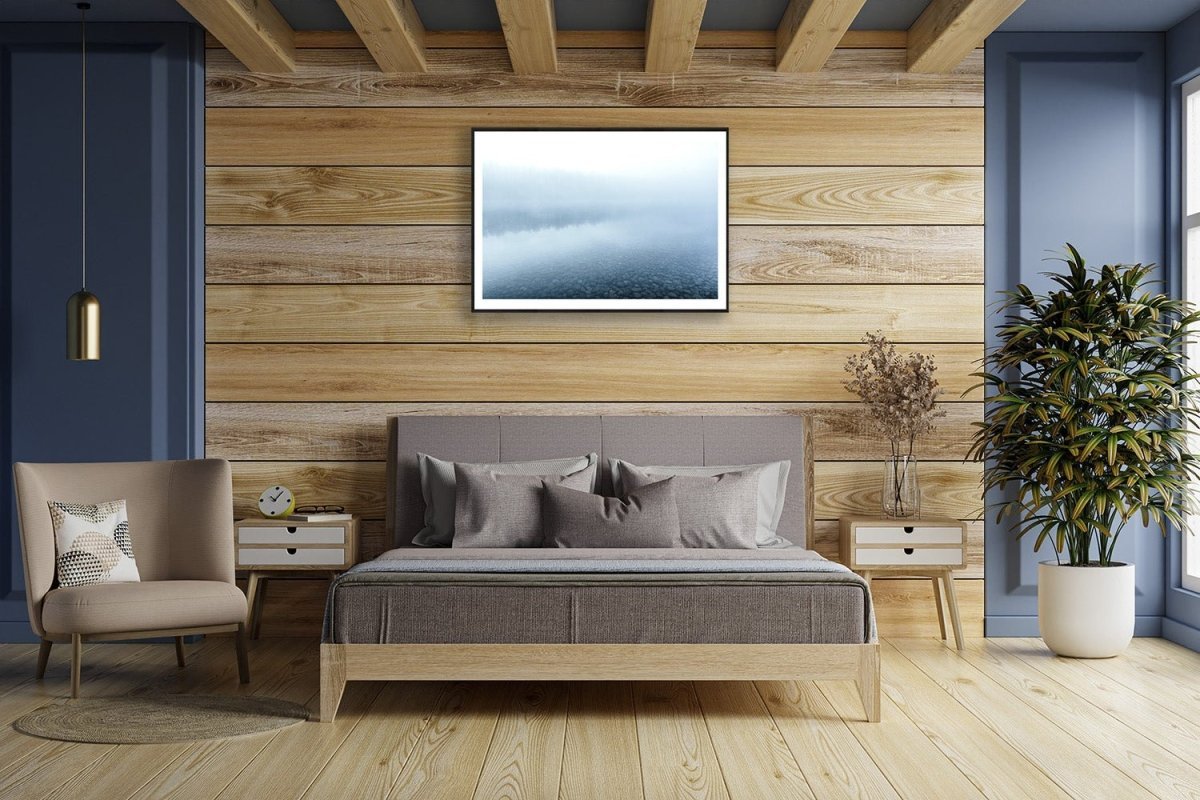 Framed blue hour photo of misty lake reflecting forest, wooden bedroom wall.