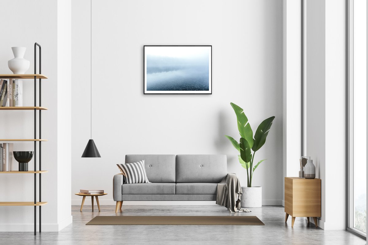 Framed blue hour photo of misty lake reflecting forest, white living room wall.