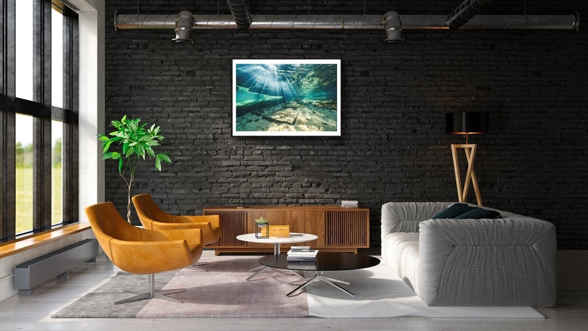 Framed photo of sunlight shining through water, illuminating underwater steps, black brick living room wall.