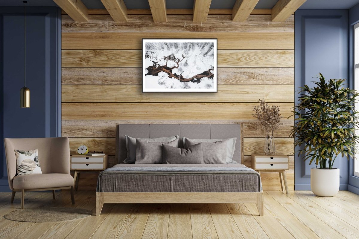 Framed photo of spring streams flowing into pond in snowy forest, wooden bedroom wall.