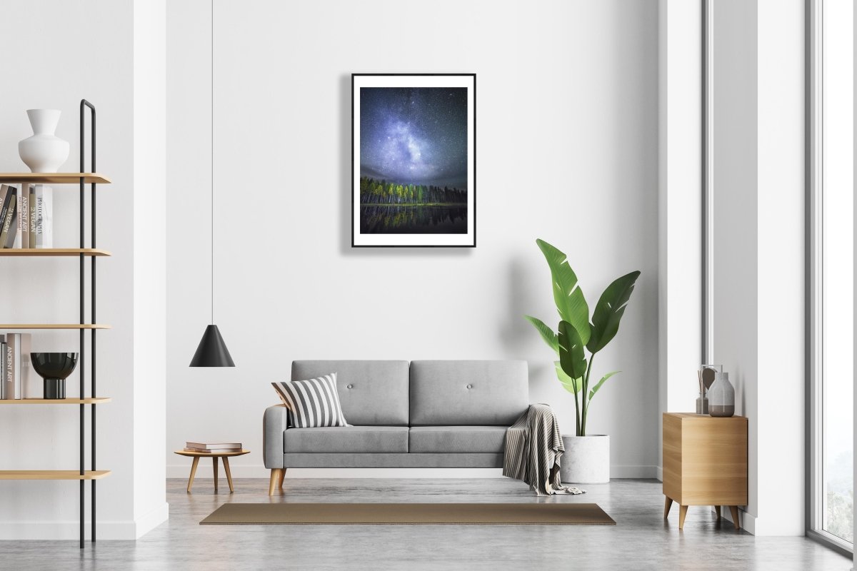 Framed photo of autumn forest reflected on tranquil water, stars and Milky Way visible, white wall.