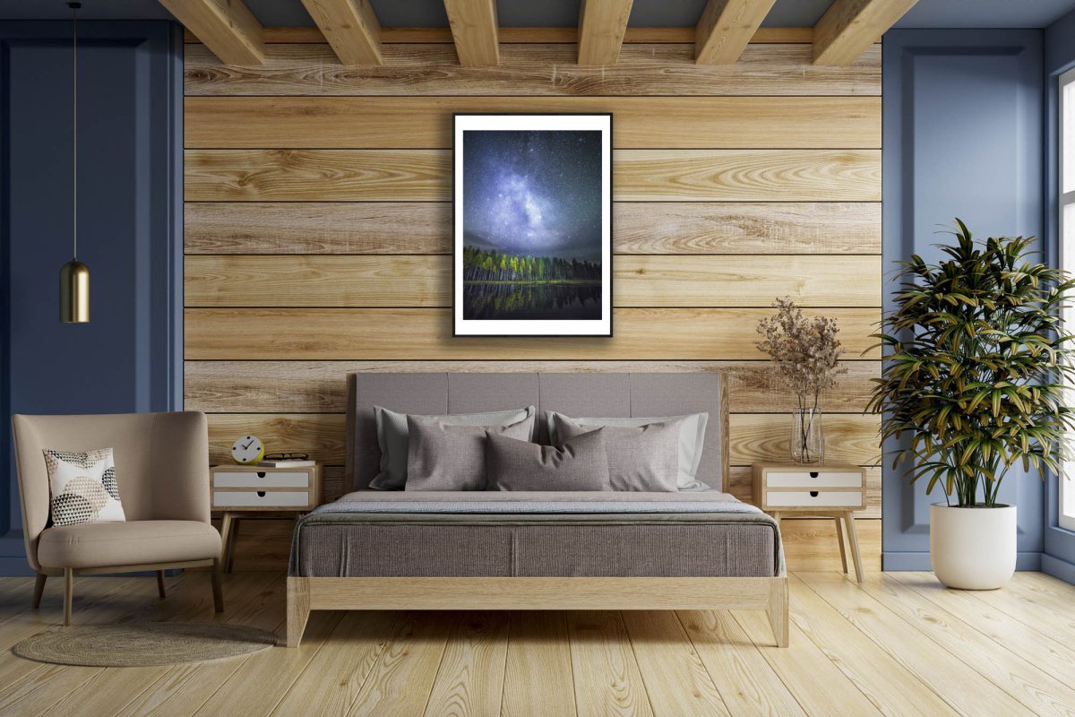 Framed photo of autumn forest reflected on tranquil water, stars and Milky Way visible, wooden bedroom wall.