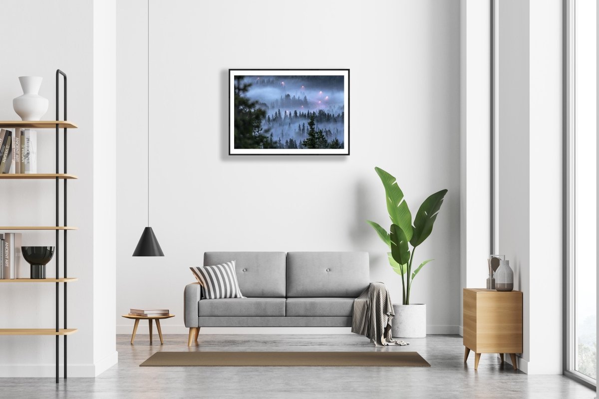 Framed photo of fog-covered forest with winding road and streetlights, landscape fading in the mist, white living room wall.